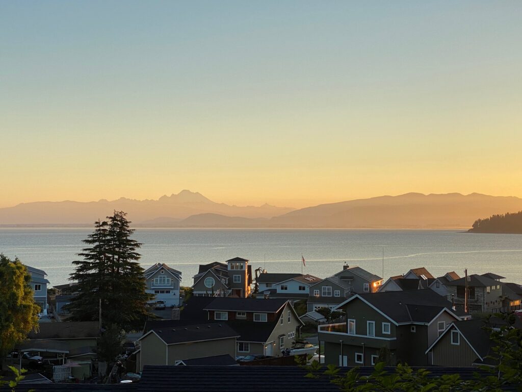 A Camano Island hillside neighborhood overlooking Puget Sound at sunset, with the silhouette of the Olympic Mountains across the water.
