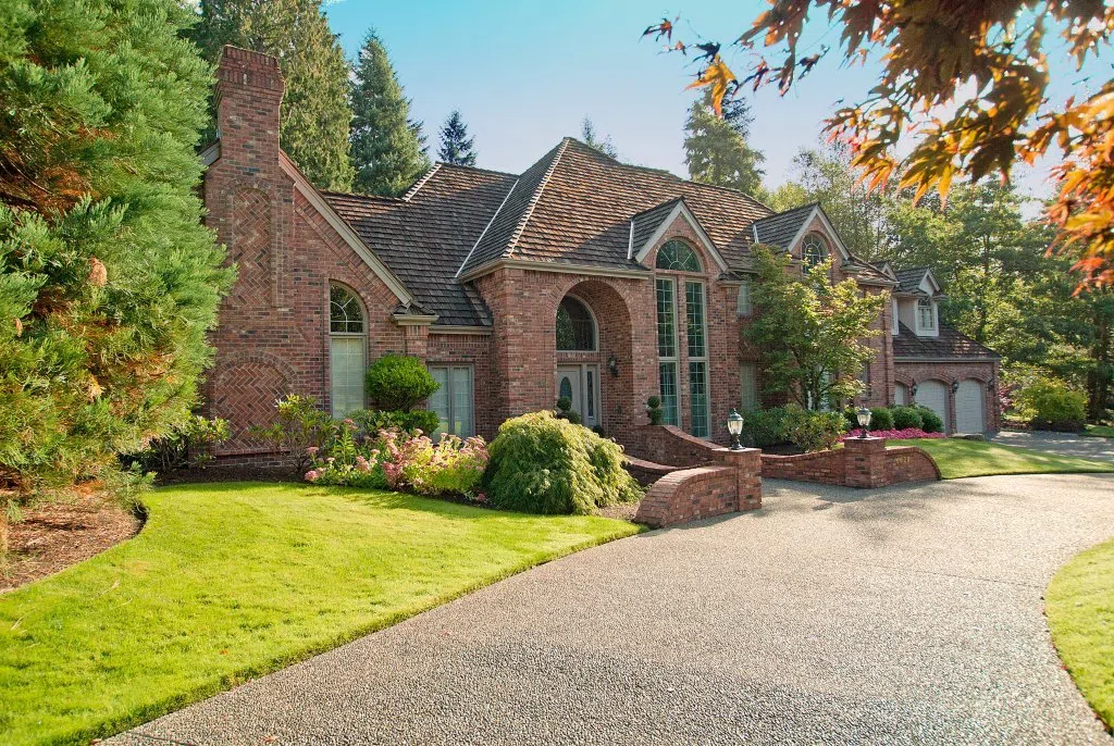 Custom red-brick European-style estate home in Woodinville’s Grousemont Estates with steep gables, arched windows, mature landscaping, and aggregate driveway.