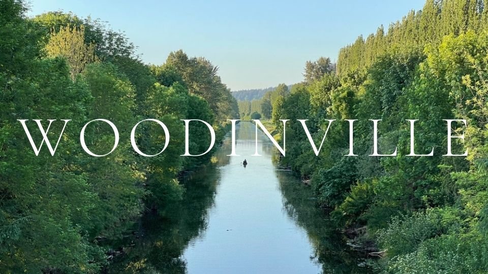 A peaceful view of a kayaker paddling down the Sammamish River in Woodinville, WA, surrounded by lush green summer trees on the Sammamish River Trail.