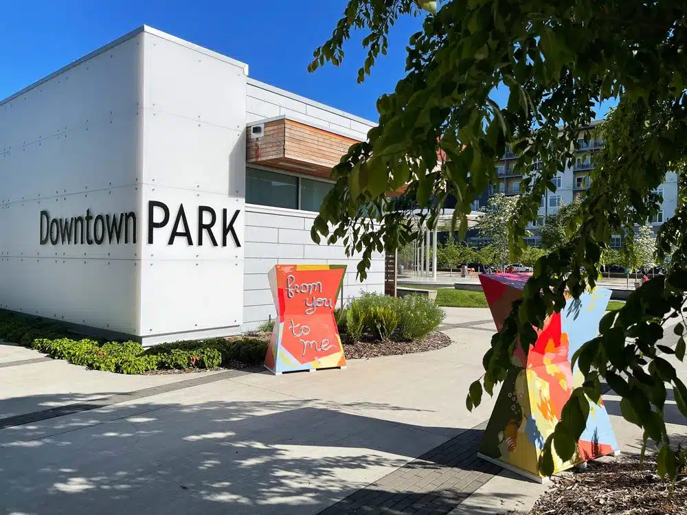 The modern Buoyant pavilion at Redmond Downtown Park, featuring a mirrored ceiling and vertical water wall rods under a clear sky.