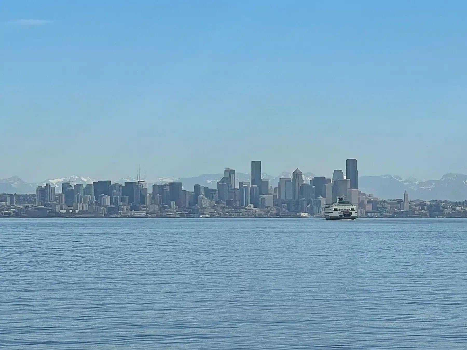 Seattle skyline view across Elliott Bay with a ferry and Cascade Mountains backdrop