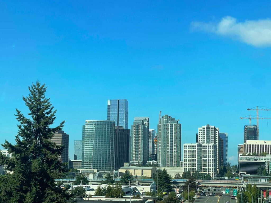 Downtown Bellevue, Washington skyline on a clear sunny day with office towers, luxury residential high-rises, and construction cranes against a vivid blue sky