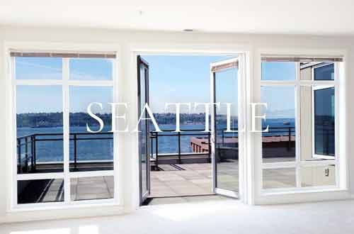Interior view of a downtown Seattle waterfront condo with floor-to-ceiling windows and open French doors leading to a deck with panoramic Puget Sound views.