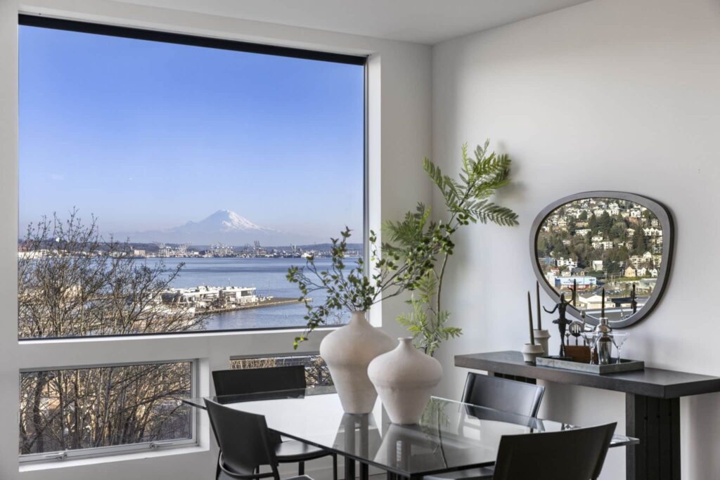 Dining area with floor-to-ceiling windows framing views of Puget Sound, the Port of Seattle, and Mount Rainier
