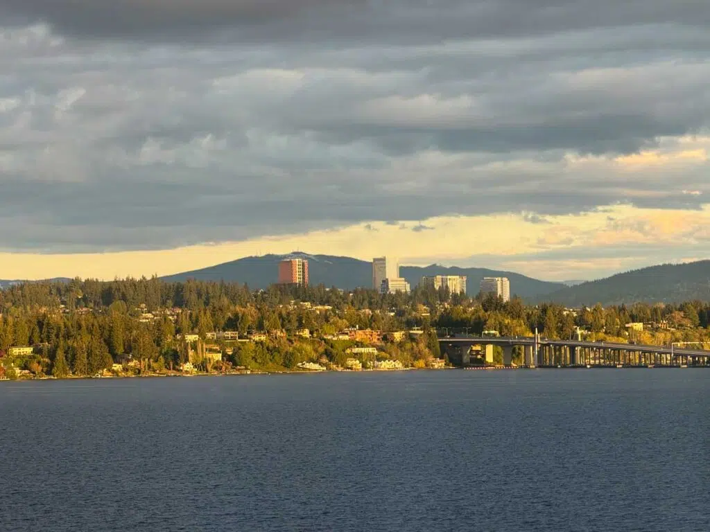 Lake Washington with the Medina shoreline, I-90 floating bridge, and Bellevue skyline backed by the Cascade foothills under dramatic storm clouds