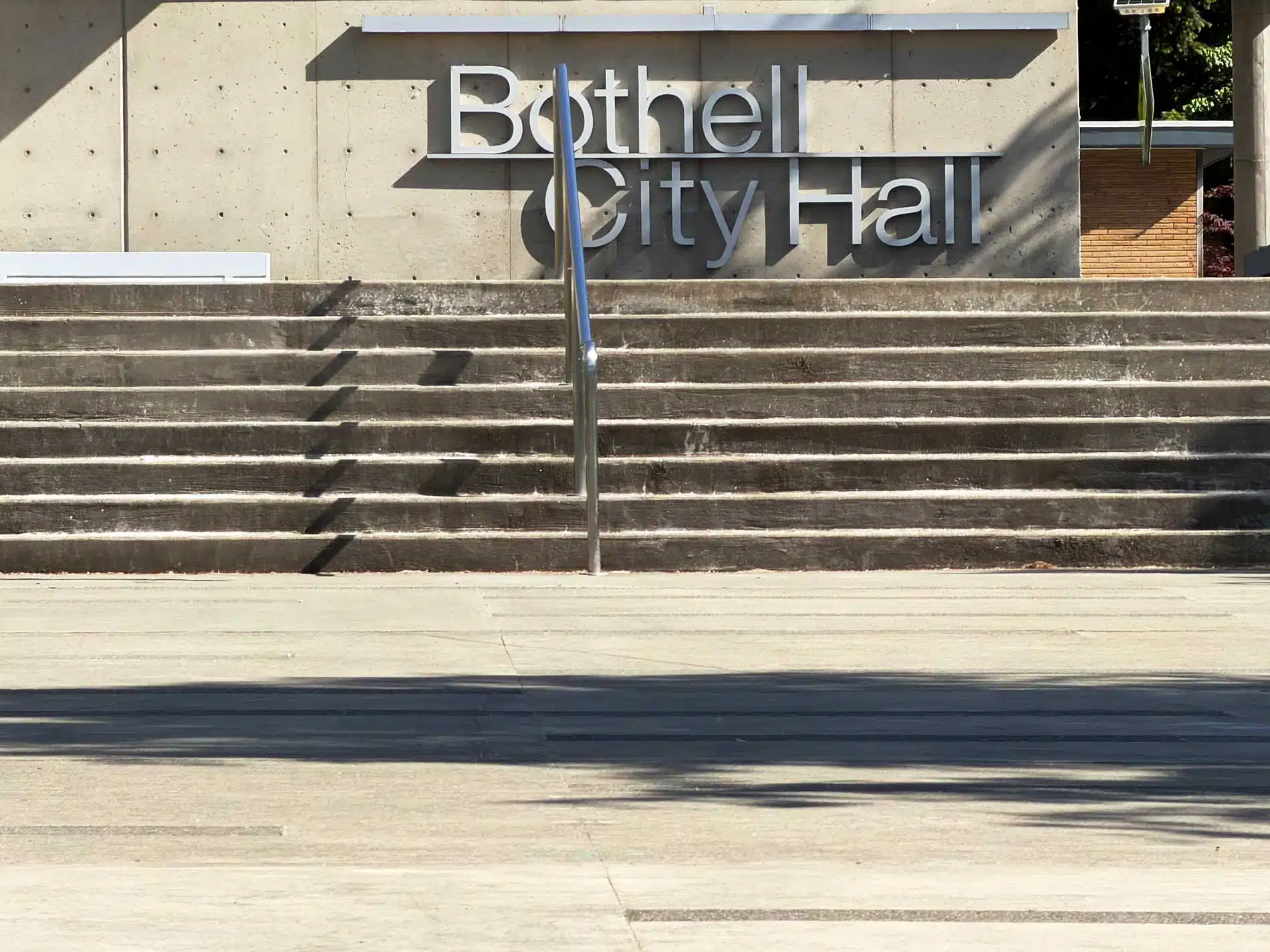 The concrete entrance steps and modern metallic exterior lettering reading "Bothell City Hall" with a silver handrail casting shadows on a sunny day.