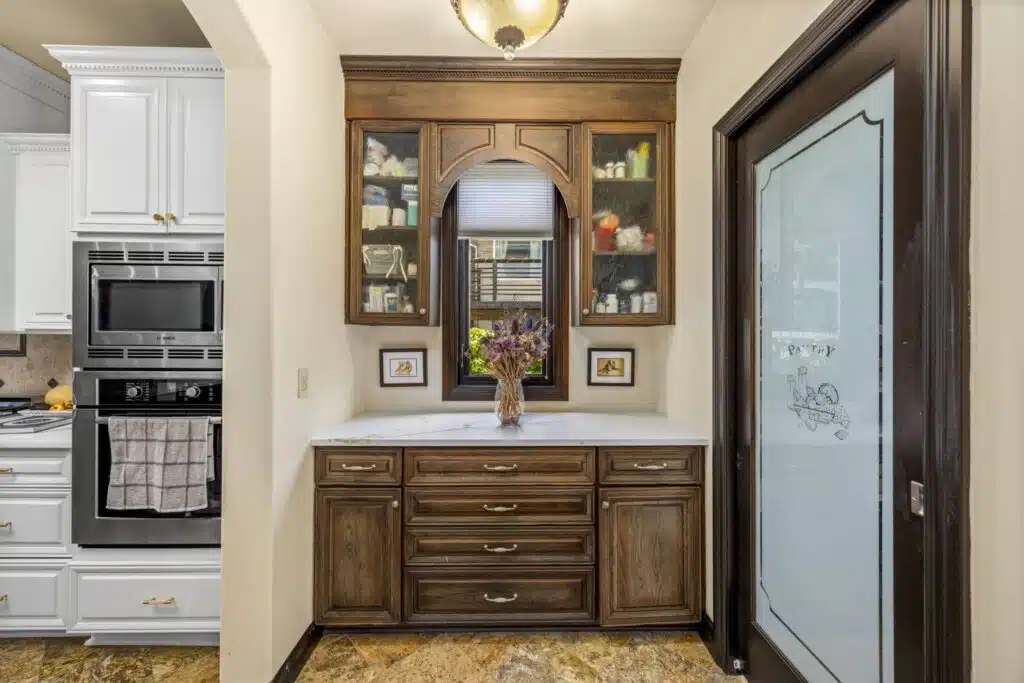 Refined Butler's Pantry with custom rich wood cabinetry, arched glass-front display cabinets, marble countertop, and dedicated walk-in pantry behind a frosted glass door.