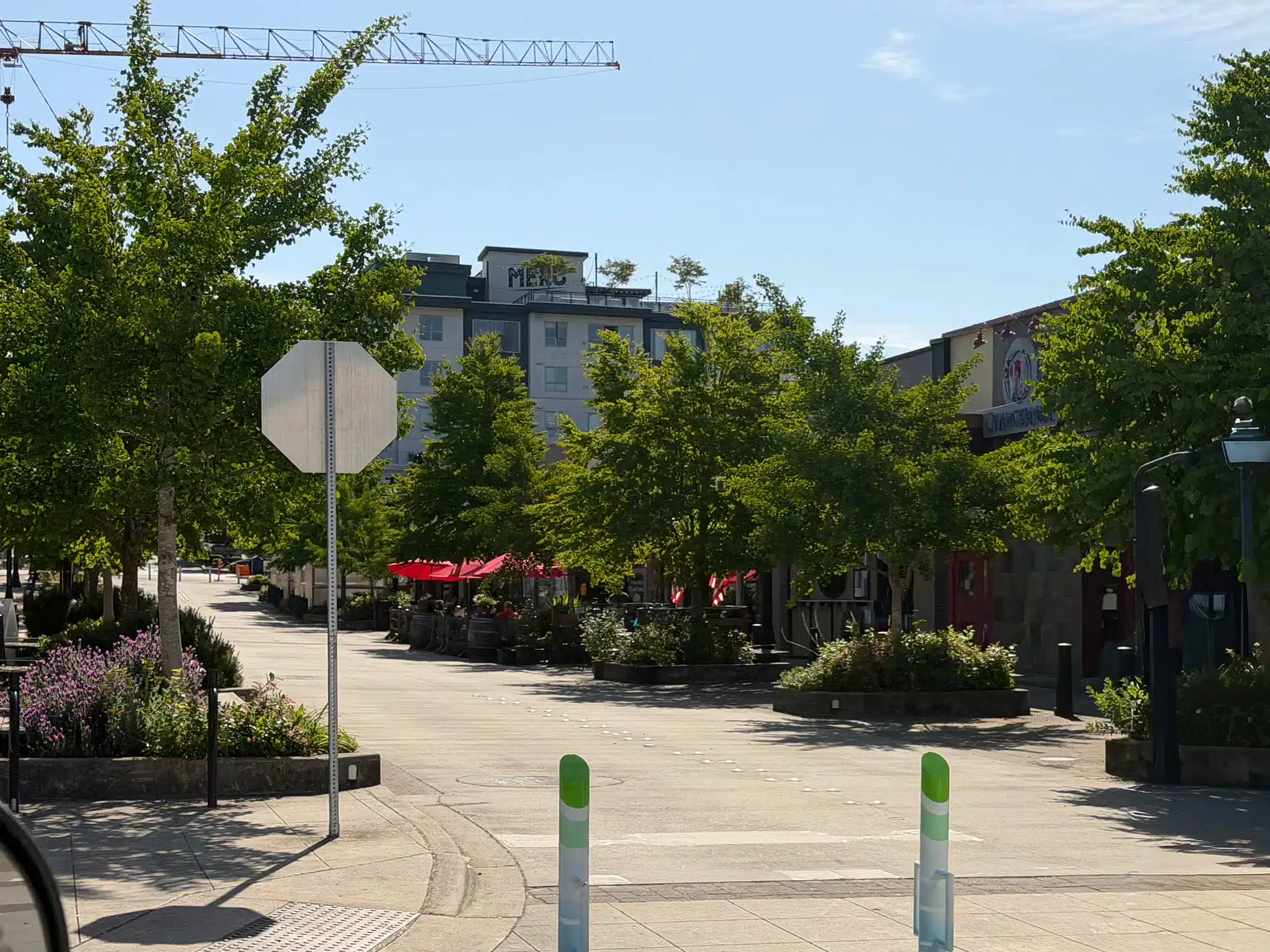 A pedestrian-friendly section of Main Street in downtown Bothell, Washington, featuring green and white bollards, a back-facing stop sign, outdoor restaurant seating with red umbrellas, and the Txokoa building in the background.
