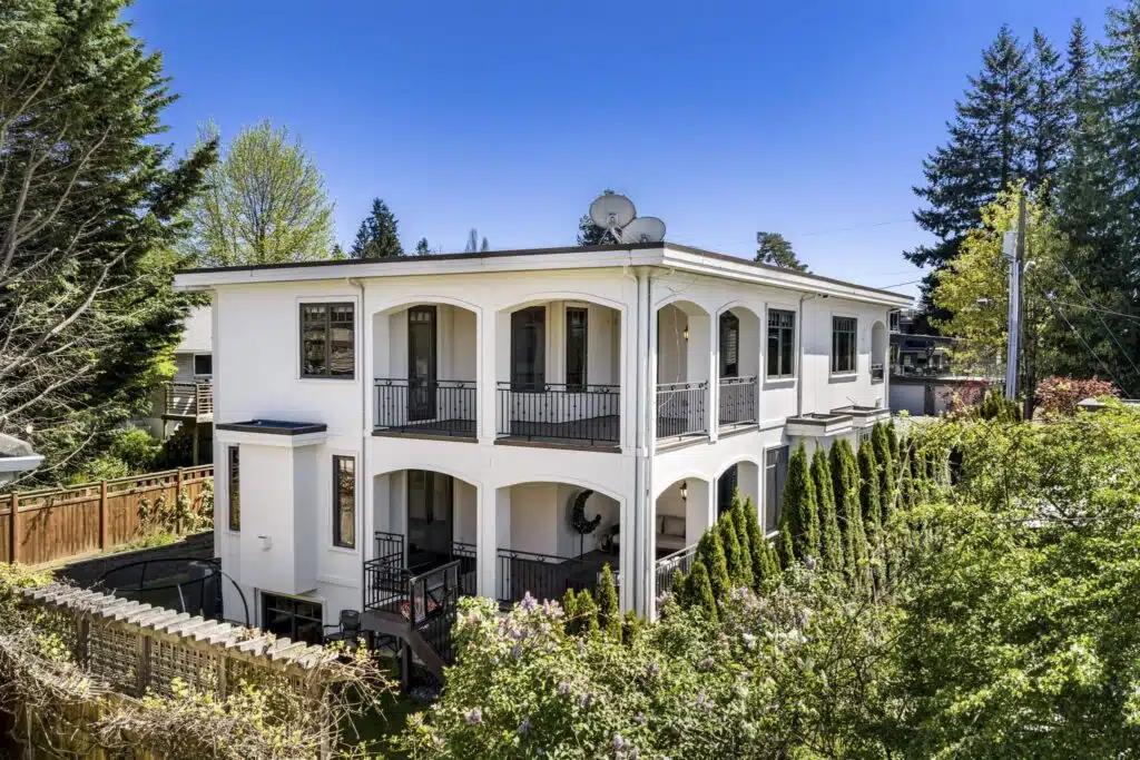 Striking rear elevation of the home with three levels of balconies, classical columns, and meticulous landscaping.