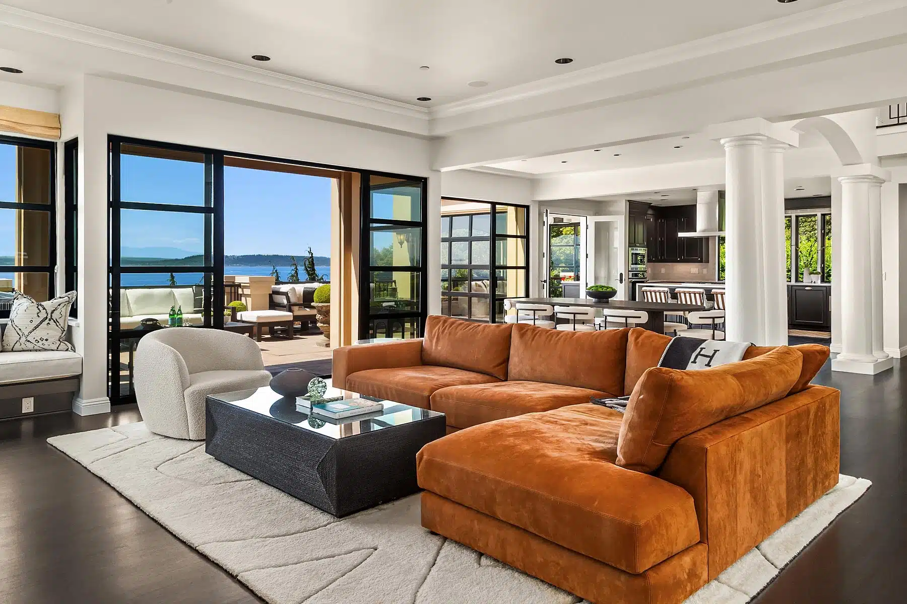 Open-concept great room with floor-to-ceiling black-framed sliding doors opening to a covered terrace and Puget Sound view at 20120 Richmond Beach Dr NW in Shorline, WA.