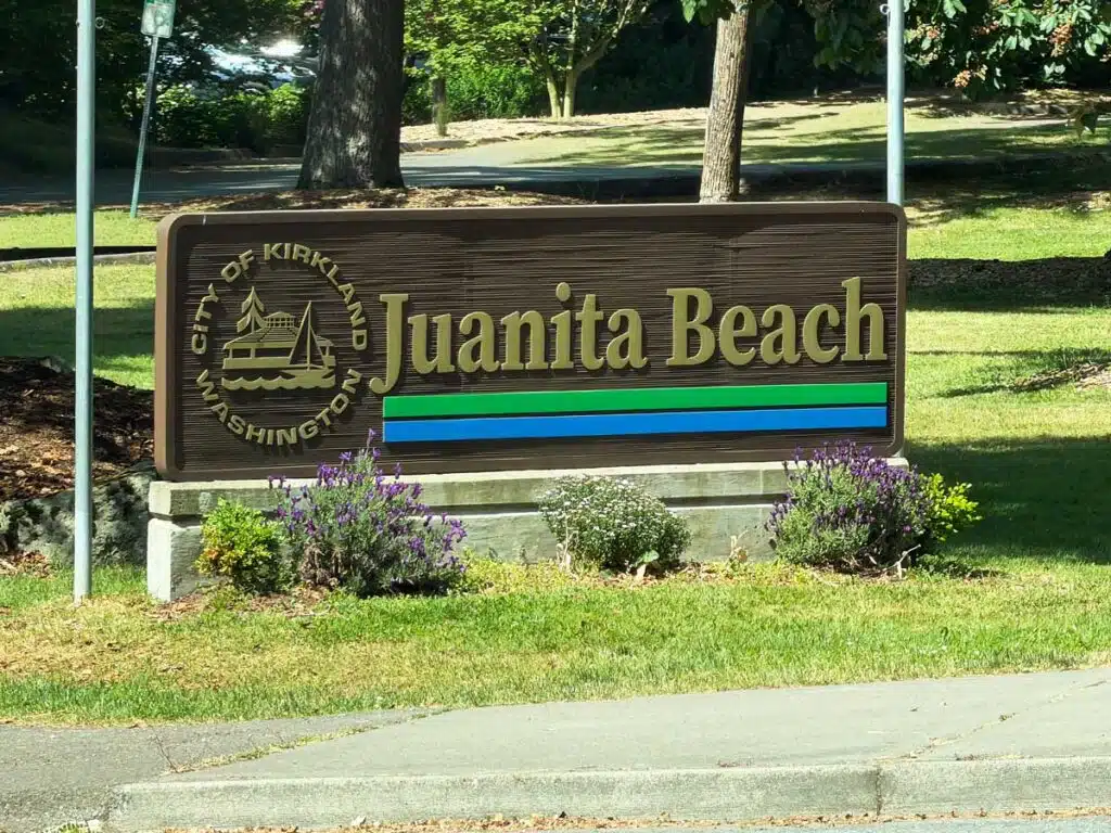 Living in South Juanita, Kirkland: 2026 Neighborhood & Real Estate Guide 1 Official City of Kirkland Washington welcome sign at the entrance of Juanita Beach Park surrounded by green grass and flowers.