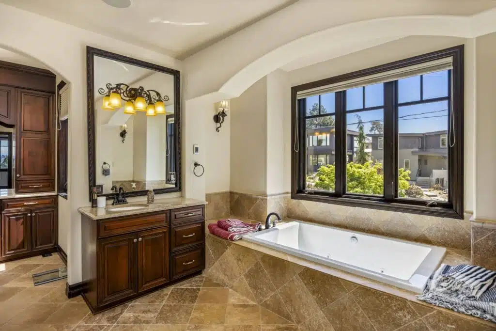 Spa-inspired Primary bath with deep soaking tub set beneath a picture window, framed by rich wood cabinetry.