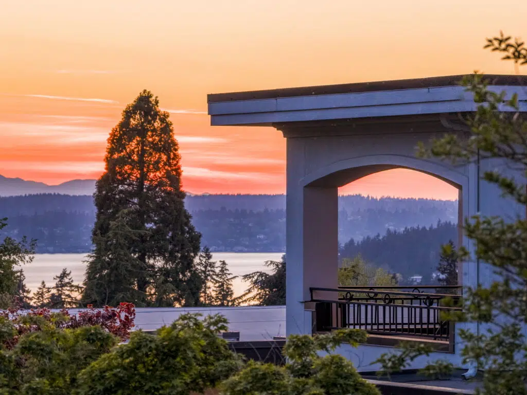 Sunset view from the Primary Suite's private balcony framed by graceful archway detailing, overlooking Lake Washington and the Olympic mountains.