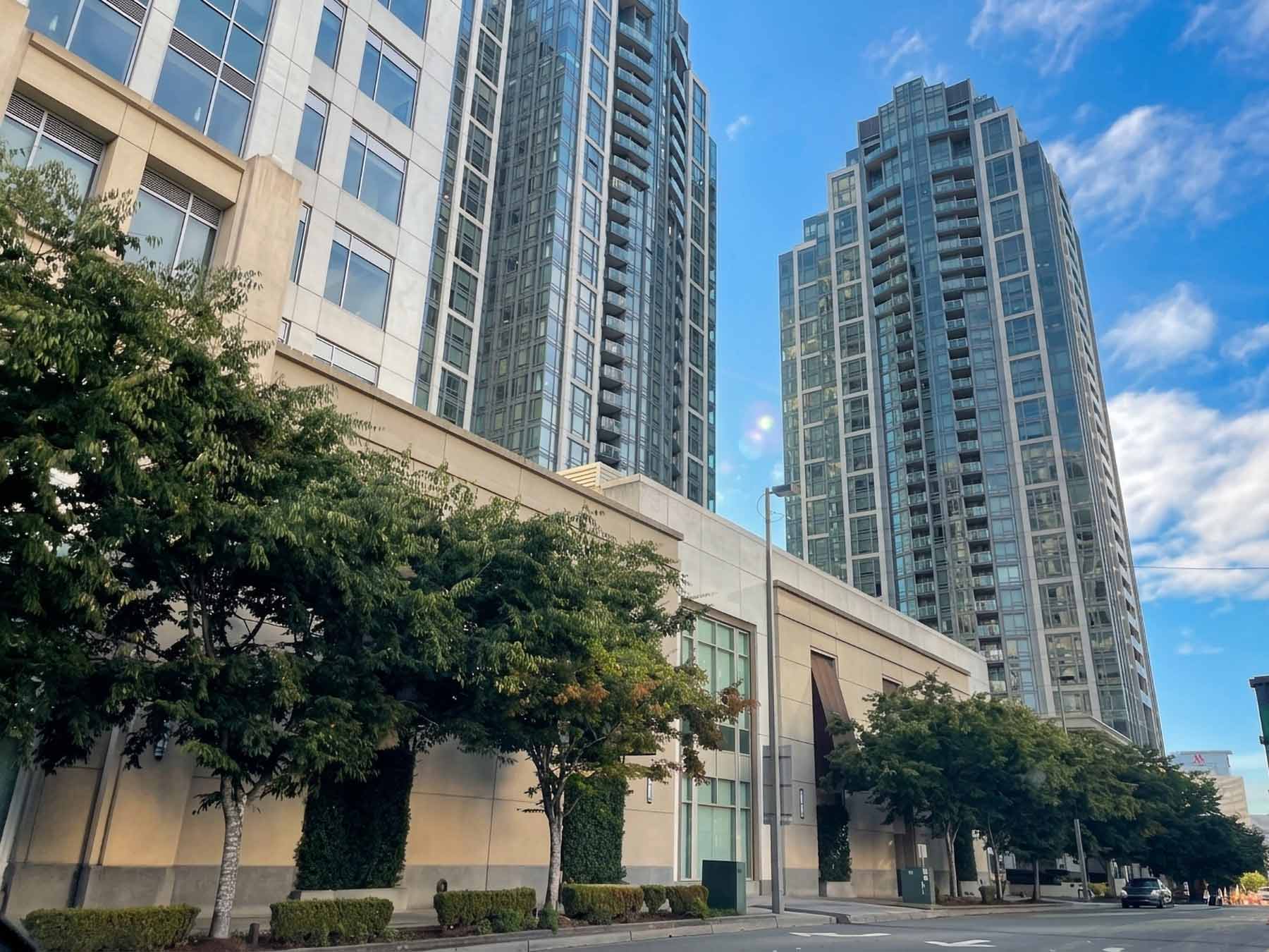 Modern glass high-rise residential towers lining a tree-shaded street in downtown Bellevue, Washington, under a clear blue sky