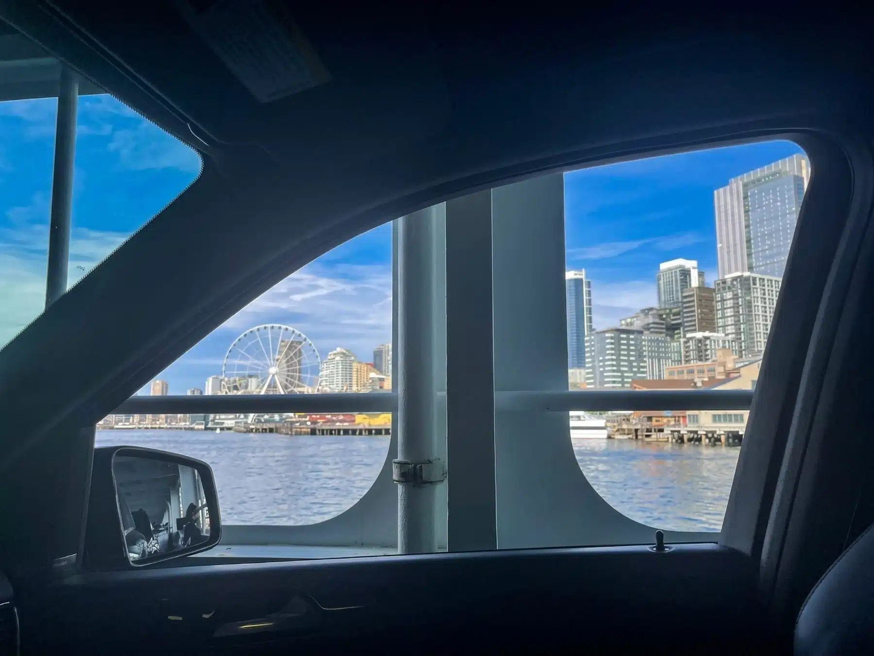 View of the Seattle waterfront, Great Wheel, and downtown skyline seen through a car window aboard a Washington State Ferry.